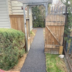 Rubber paved walkway next to a house through a gate in the fence