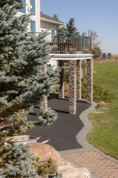 Rubber paved patio on bottom level of a home with rock columns to a deck above